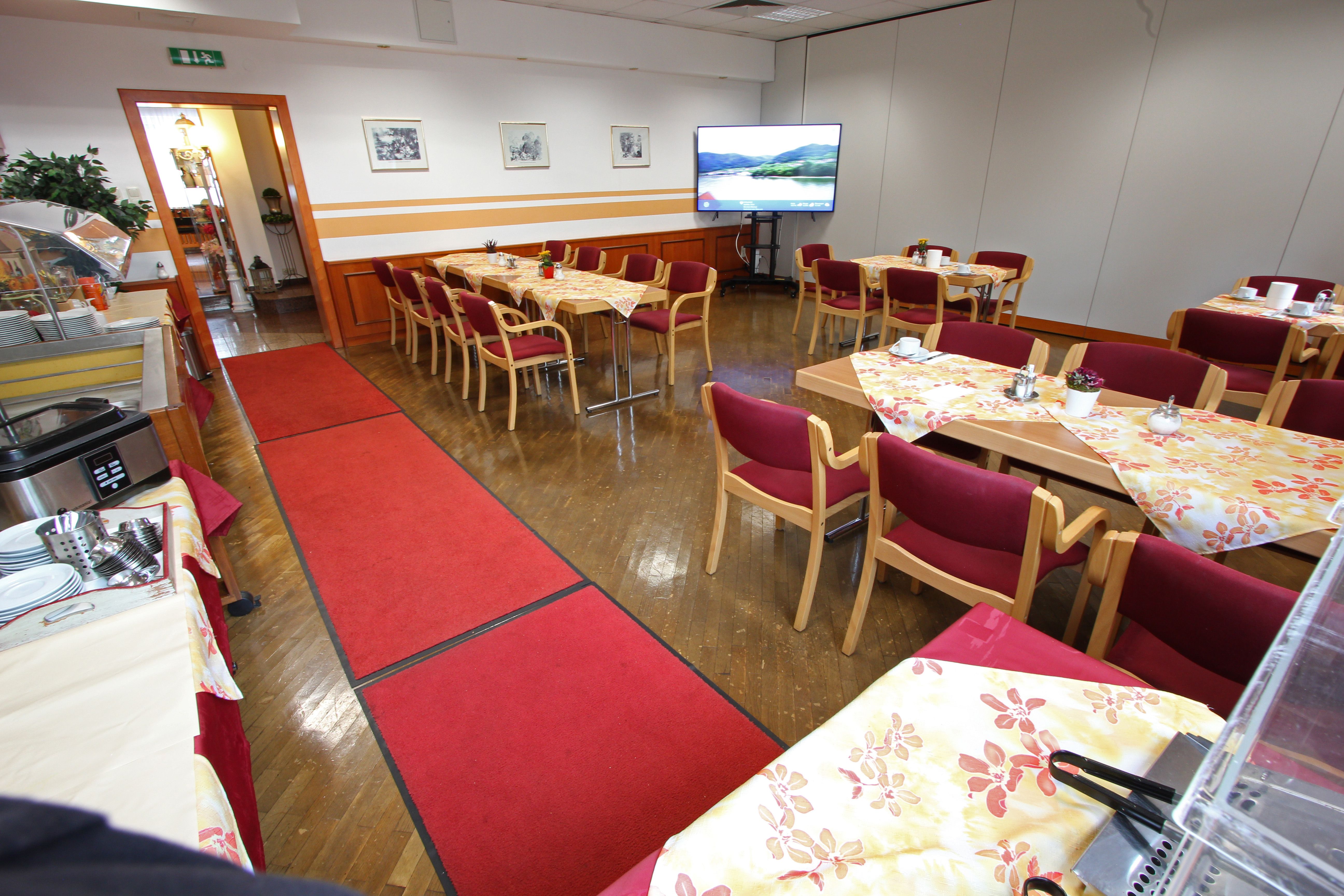 Ein Konferenzraum mit gedeckten Tischen, roten Stühlen und einem großen Bildschirm.