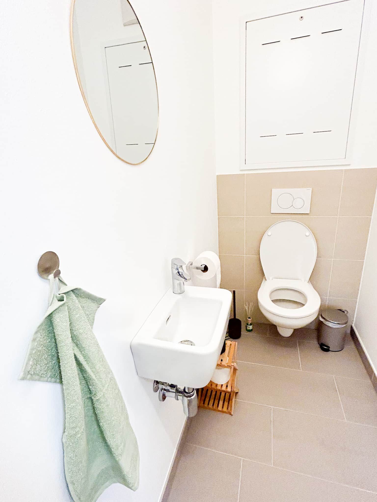 Large, bright WC with beige tiles, washbasin, towel and waste garbage can