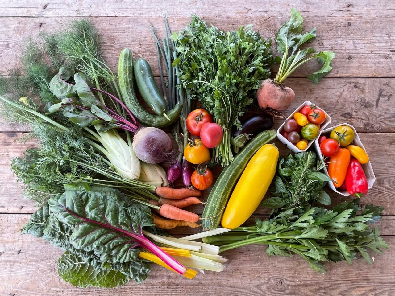 Bunte Gemüsesorten und diverse Kräuter auf einem Holztisch.