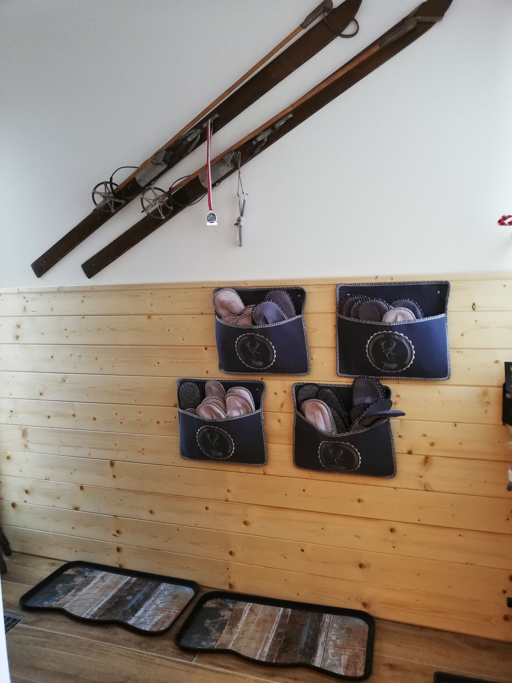 Eingangsbereich mit Holzverkleidung, alten Skiern an der Wand und Filzpantoffeln in Taschen.