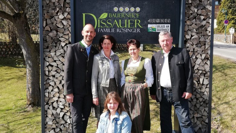F&uuml;nf Personen vor einem Schild mit der Aufschrift 'Bauernhof Dissauer Familie Rosinger'.