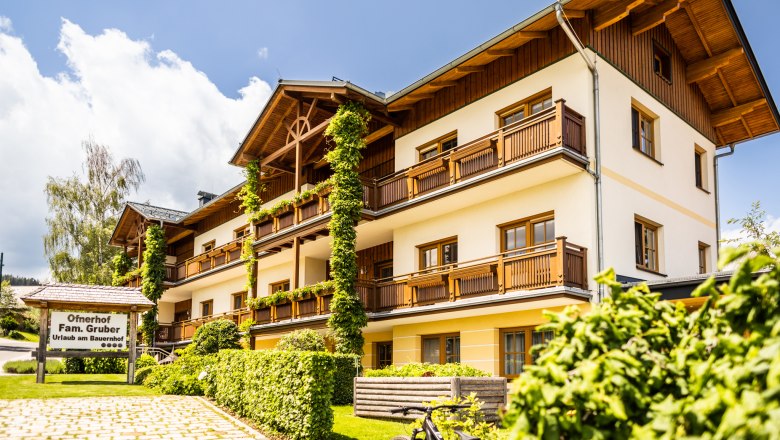 Vorderansicht des Ofnerhof, großer Gasthof mit gelber Fassade mit Holzverkleidung und Balkone