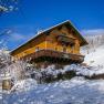 Ein Holzhaus im Schnee mit blauem Himmel im Hintergrund.