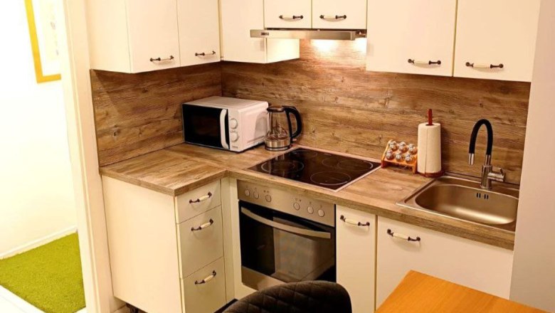 Moderne K&uuml;che mit Holzarbeitsplatte, wei&szlig;en Schr&auml;nken, Mikrowelle, Herd und Sp&uuml;le.