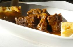 Tiefer weißer Teller mit geschmortem Wildschweinbraten, soße und Beilagen.