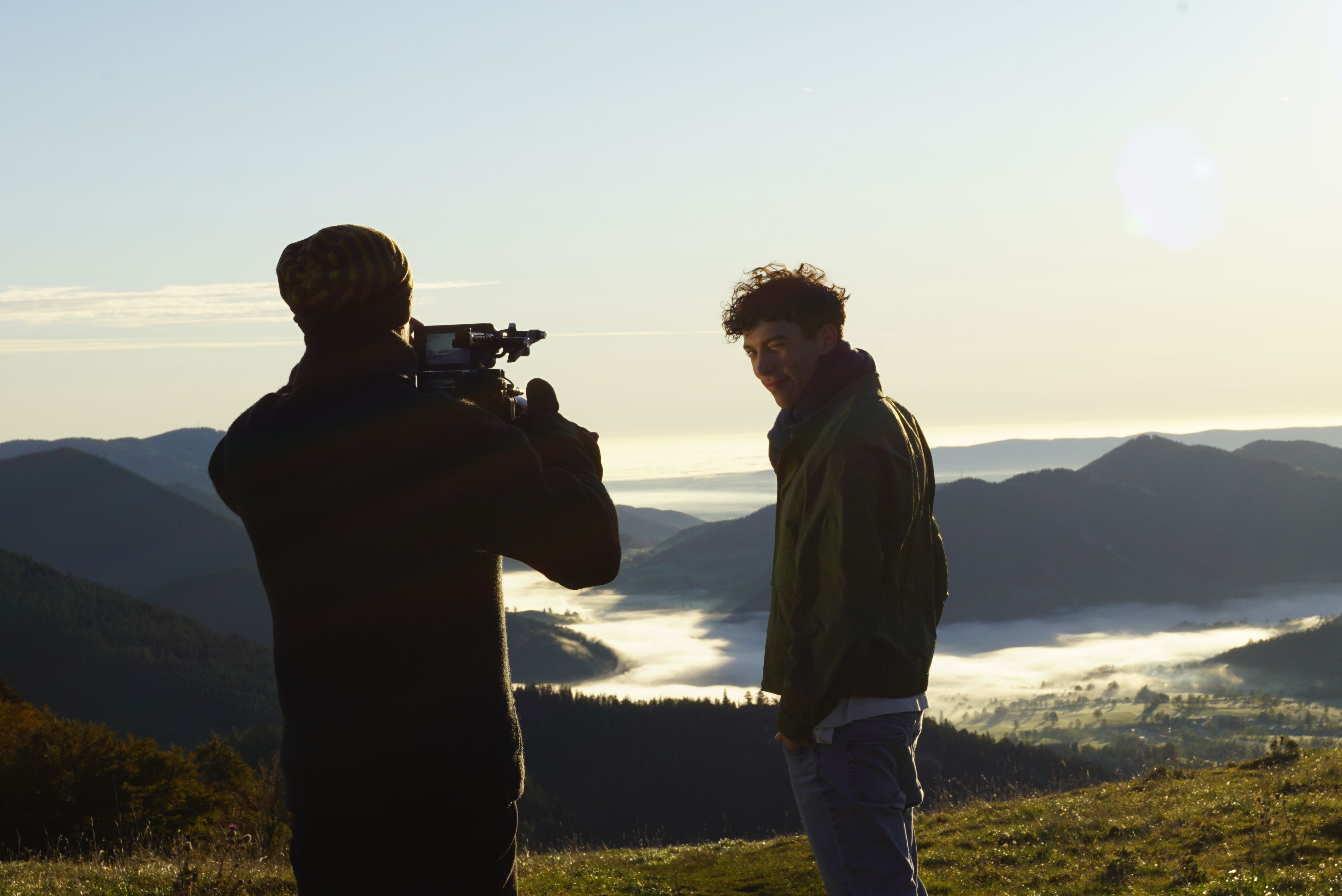 Bei Dreharbeiten wird der Darsteller vor alpinen Panoramaausblick vom Berg mit Nebel in den Tälern vom Kameramann gefilmt.
