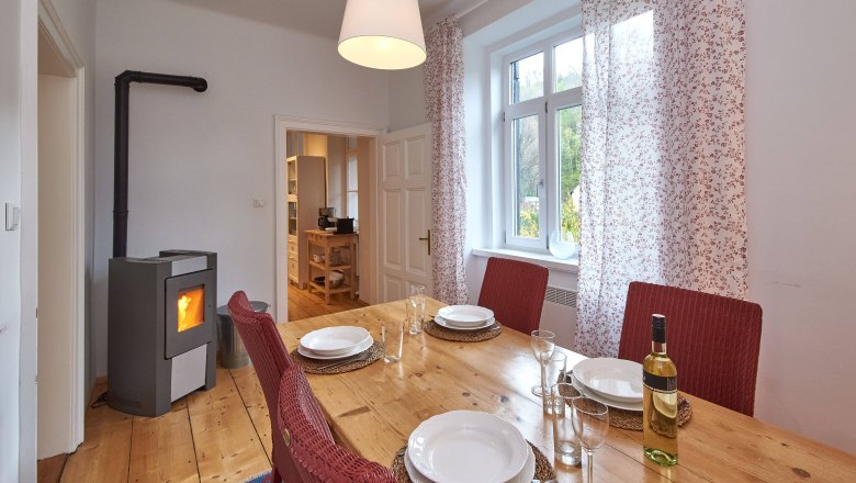 Esszimmer mit Holztisch, roten Stühlen, gedecktem Tisch und Kaminofen.