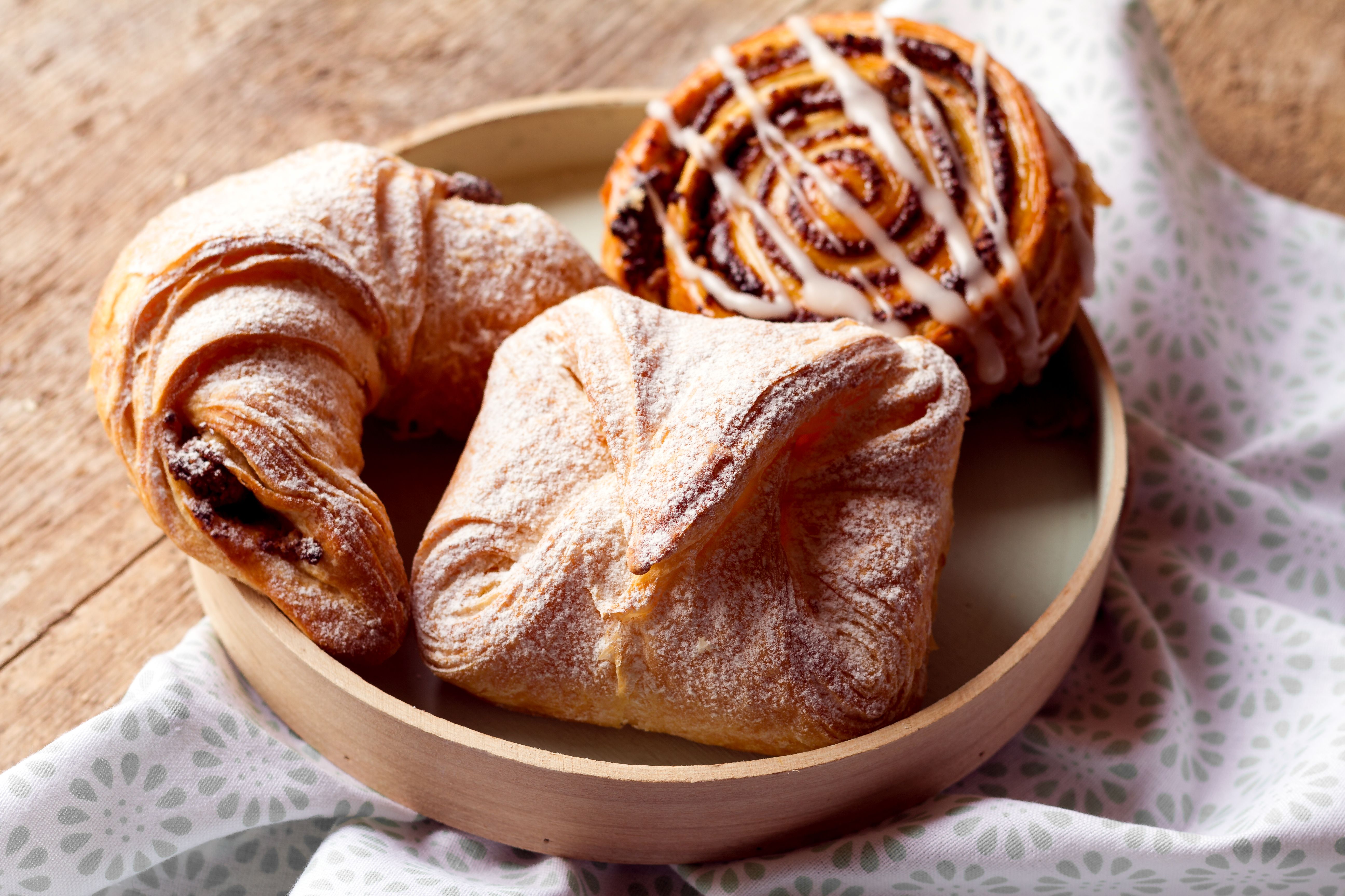 Ein Nusskipferl, eine Topfengolatsche und eine Mohnschnecke in einem Holztablett auf einem grün-weißen Tuch.