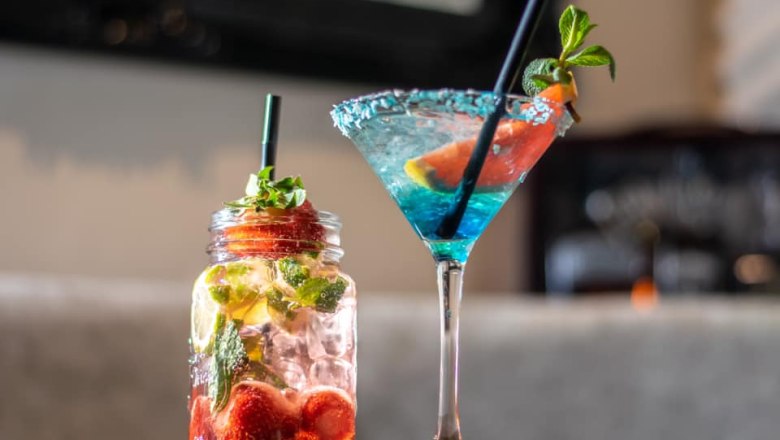 Zwei Cocktails, einer in einem Einmachglas mit Erdbeeren und Minze, der andere in einem Martiniglas mit blauer Fl&uuml;ssigkeit und Zitrusfrucht.