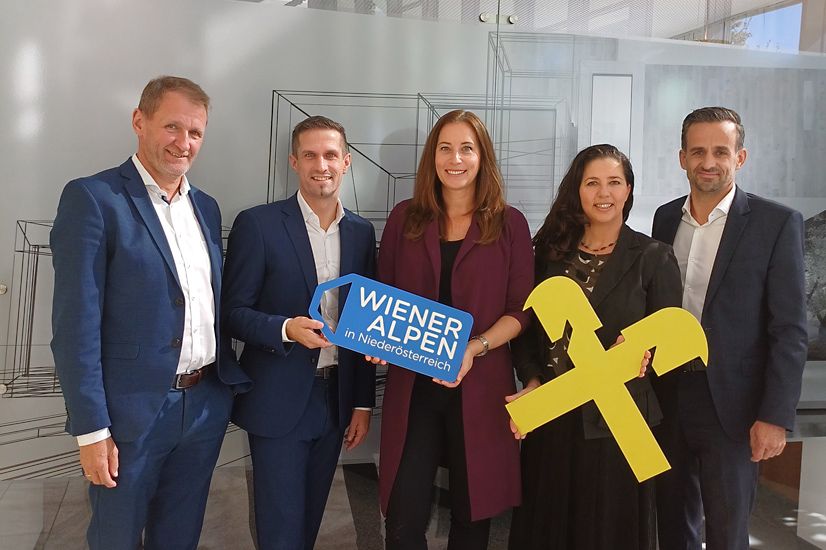 Fünf Personen der Wiener Alpen in Niederösterreich & Raiffeisenbank Region Wiener Alpen stehen nebeneinander und halten ein Wiener Alpen-Logo Schild sowie ein Raiffeisenbank-Logo Schild in den Händen. 