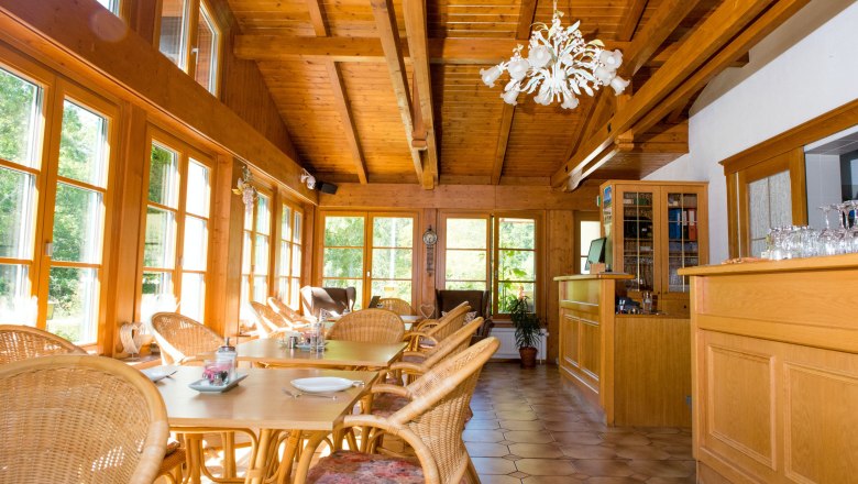 Ein heller Fr&uuml;hst&uuml;cksraum mit Holzm&ouml;beln, gro&szlig;en Fenstern und einem Kronleuchter.