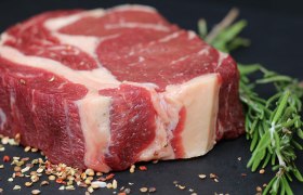 A raw steak on a dark plate decorated with spices and herbs.