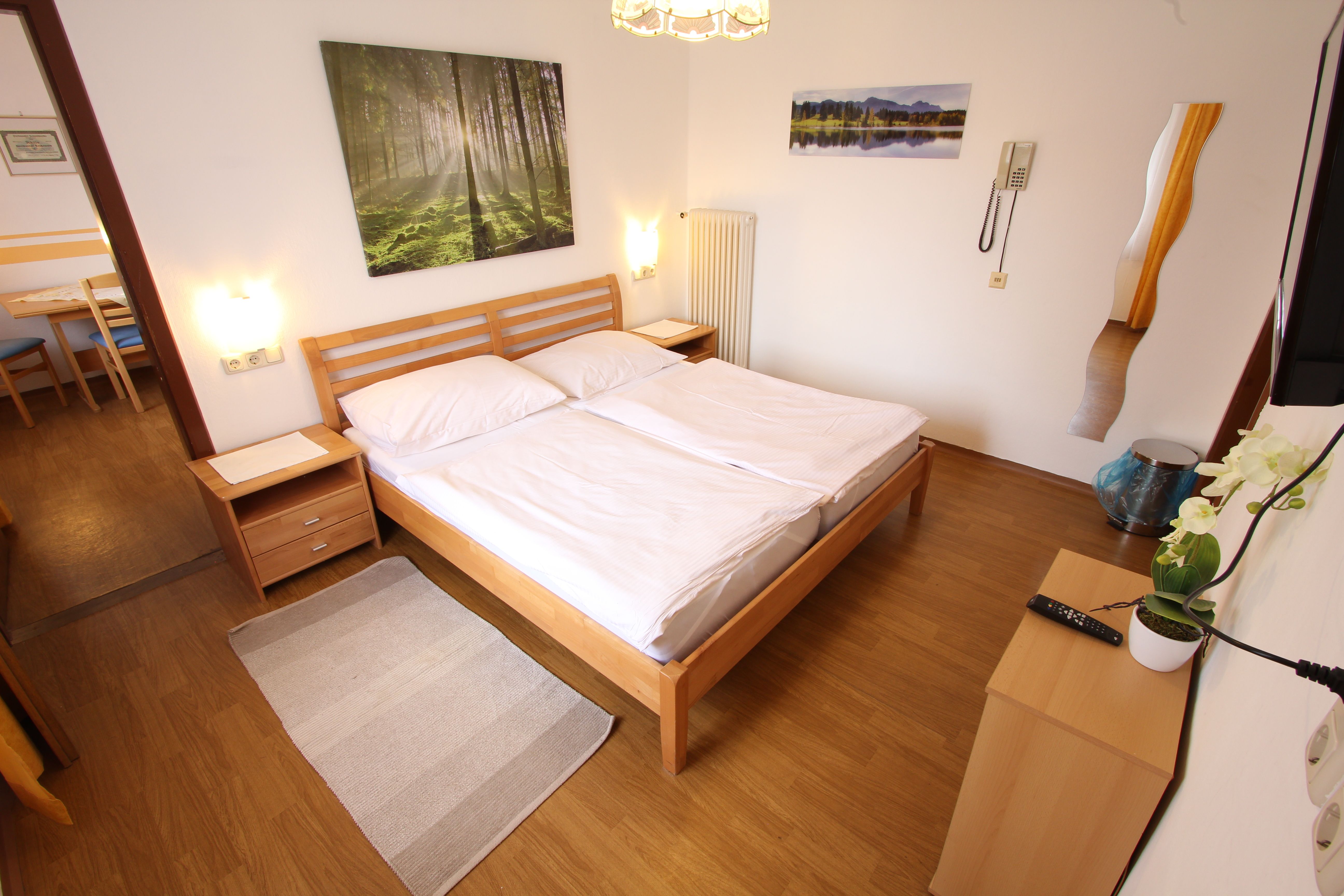 Helles Schlafzimmer mit Doppelbett, Holzmöbeln und Naturbildern an der Wand.