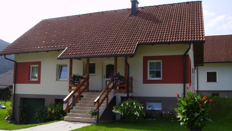 Ein Einfamilienhaus mit rotem Dach und weiß-roter Fassade, umgeben von gepflegtem Garten und Blumen.