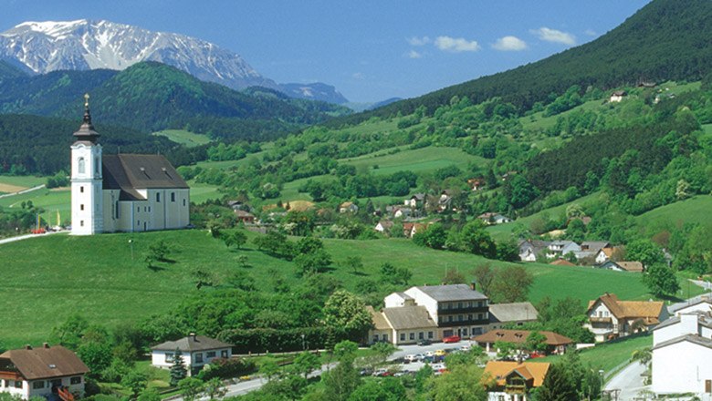 Landscape with a church on a hill, surrounded by green fields and mountains in the background.