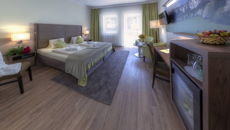 Elegant hotel room with double bed, seating area and large window.