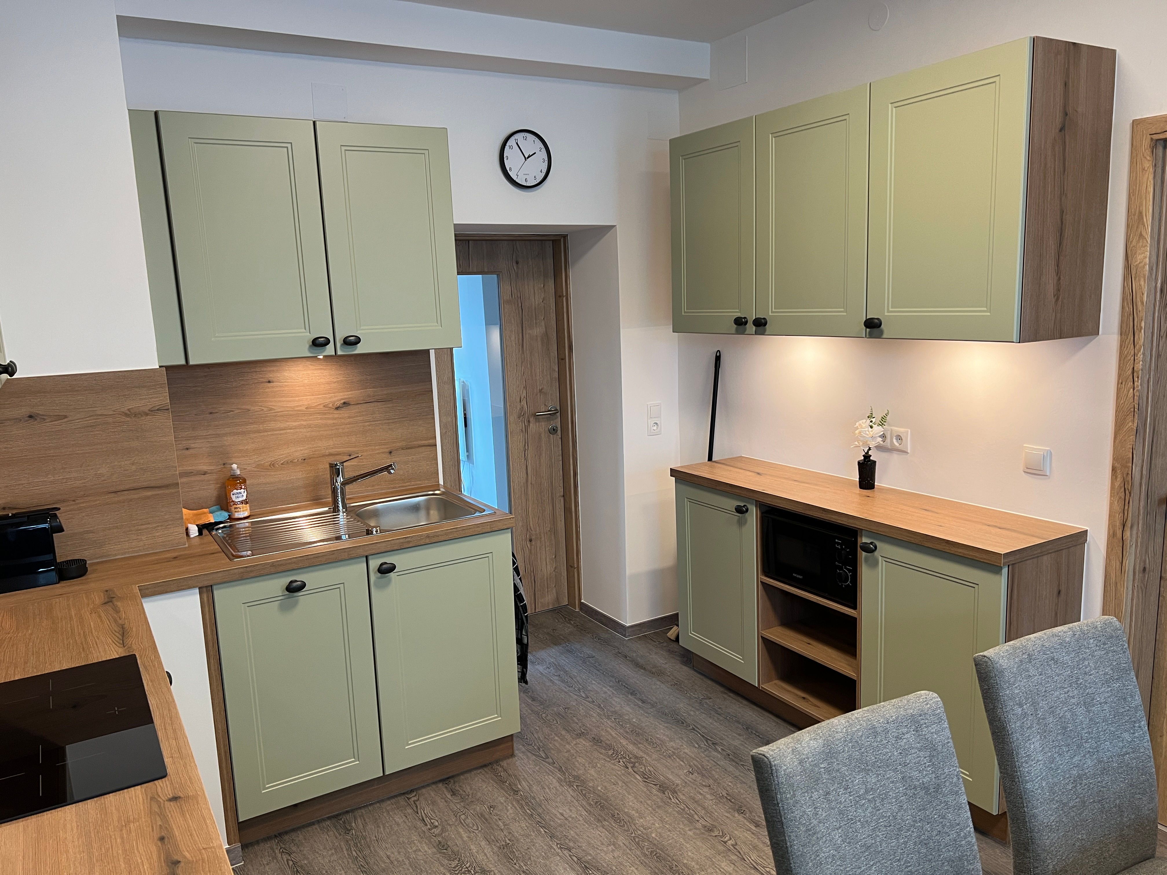 Moderne Küche mit grünen Schränken, Holzarbeitsplatten und grauen Stühlen.