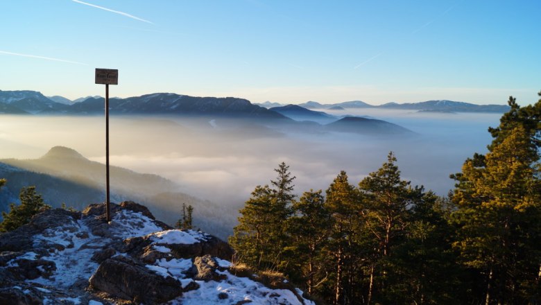 Blick von einem Berggipfel mit Nebel in den Tälern und einem klaren Himmel.