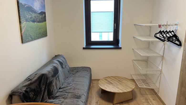 Small room with sofa, round wooden table, wall shelf and window.