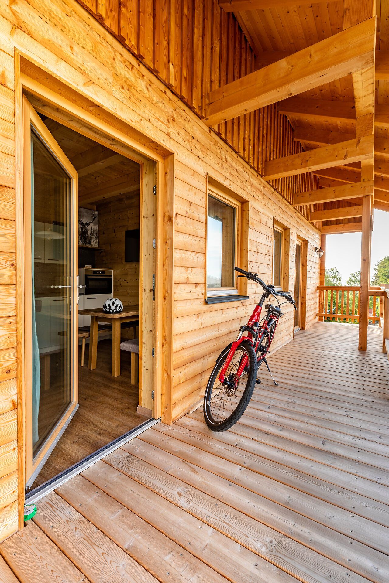 Ein Fahrrad parkt auf der Holzterrasse vor der holzvertäfelten Ferienwohnung des Sonnenhof Hechtl. Eine halboffene Terrassentür erlaubt einen Blick nach innen. 