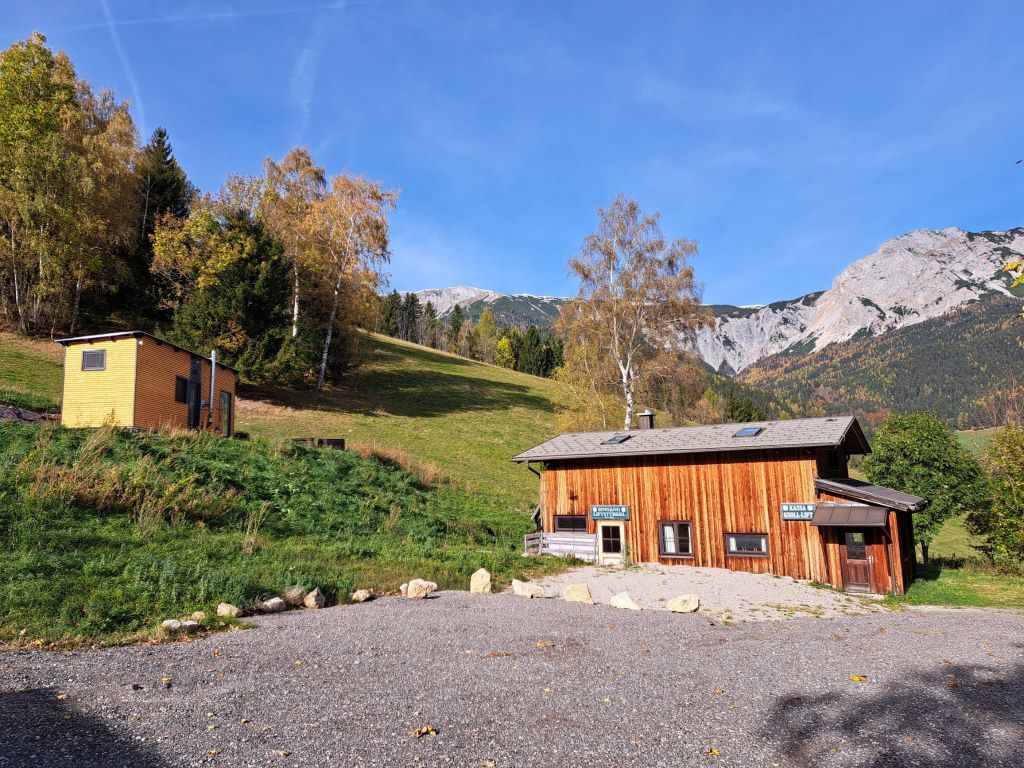 Zwei Holzhütten vor einer Berglandschaft mit blauem Himmel.