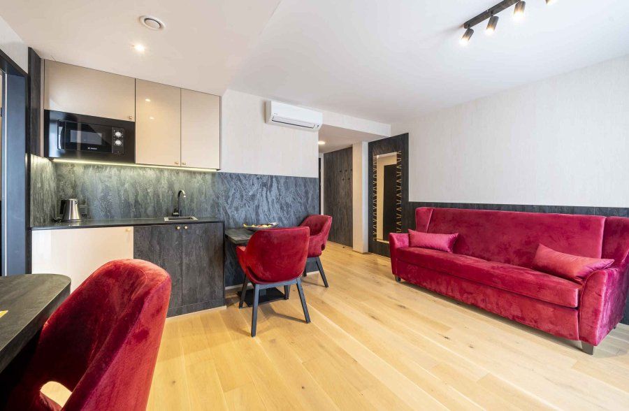 Modernes Apartment mit rotem Sofa und Stühlen, kleiner Küche und Holzboden.
