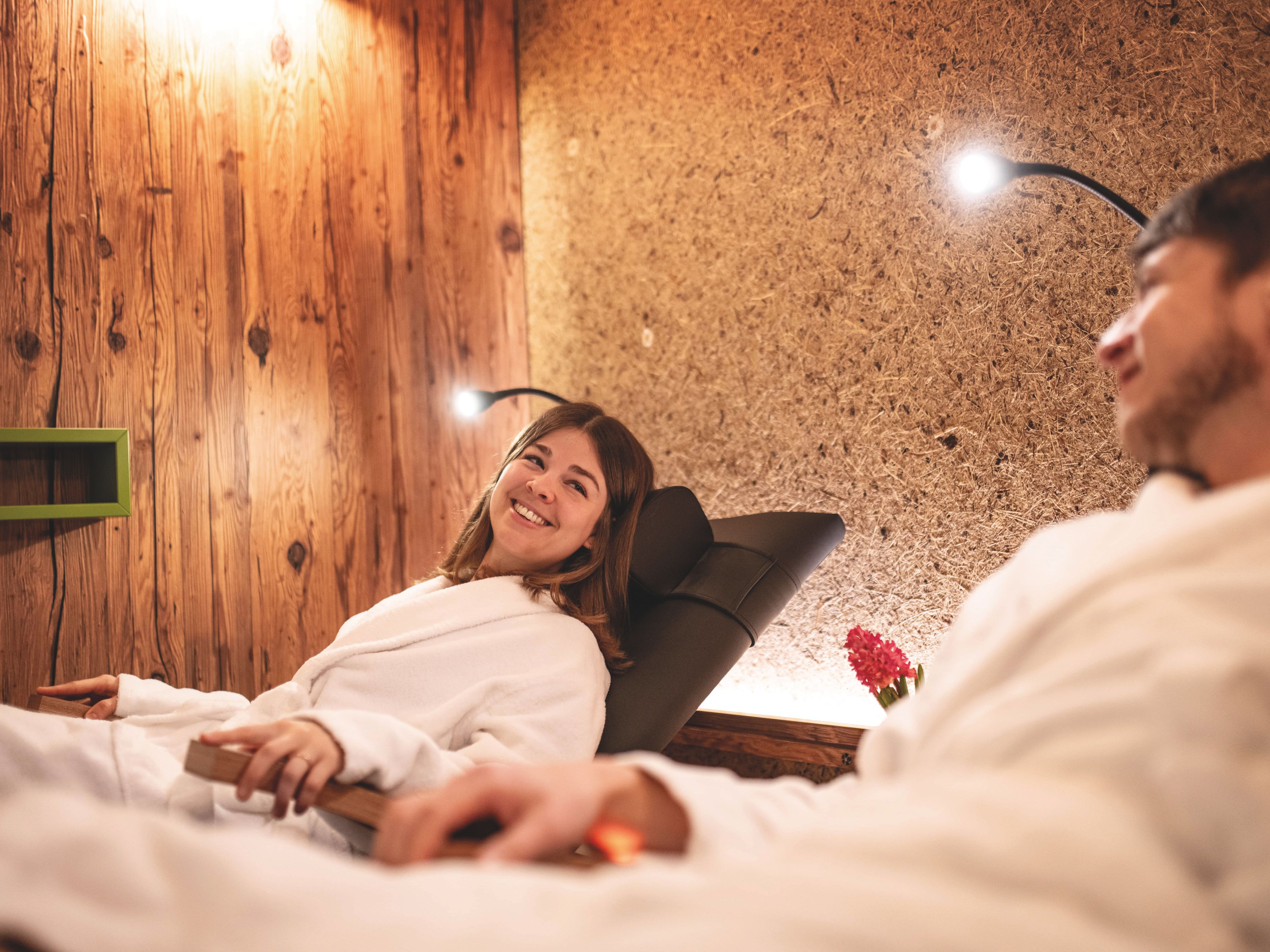Eine Frau und ein Mann in Bademänteln auf modernen Liegen in einem Wellnessbereich.