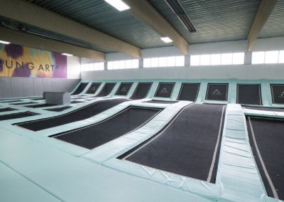 Innenansicht eines Trampolinparks mit mehreren Trampolinen in einer Halle.