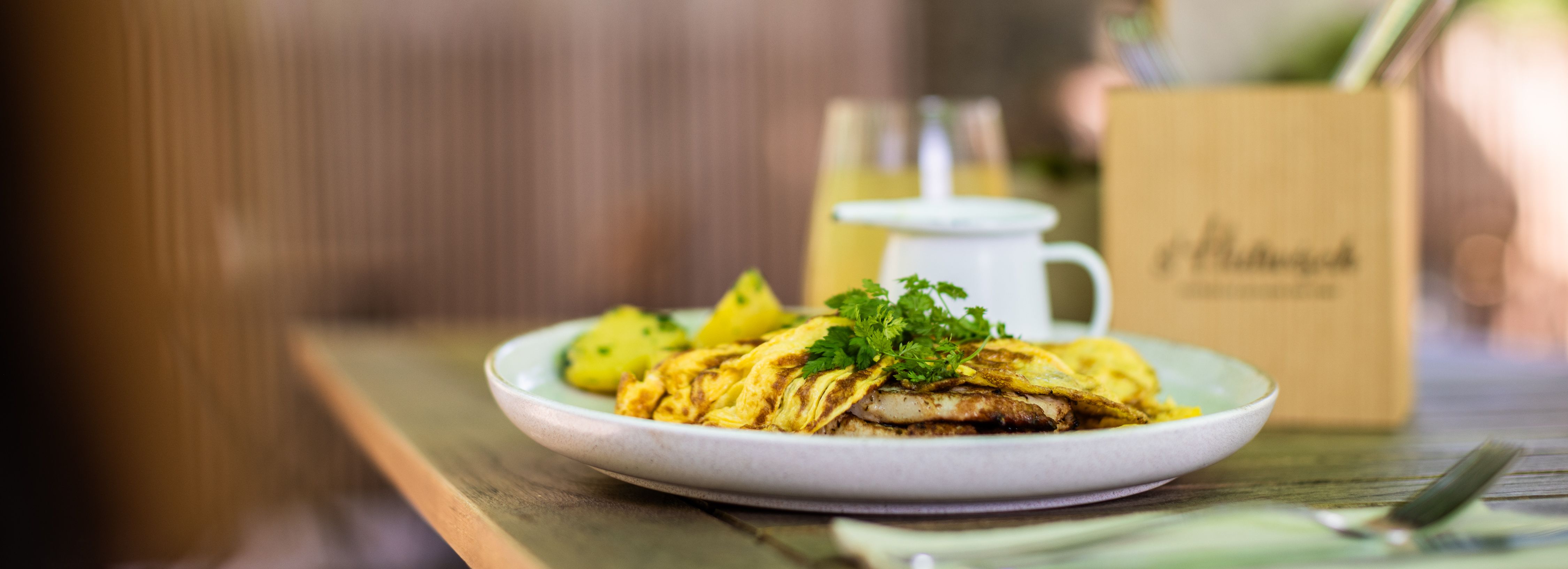 Ein Teller mit einem Gericht auf einem Tisch im Freien, daneben Besteck und Deko.