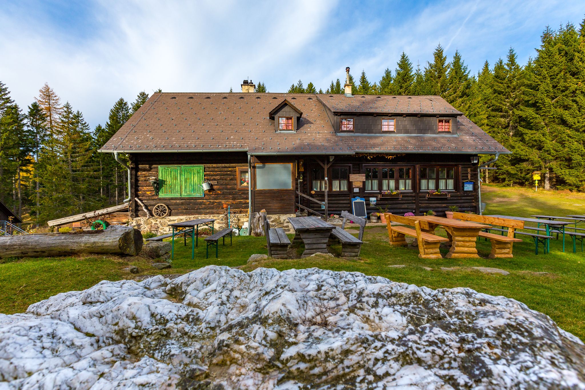 Holzhütte mit Tischen im Freien, umgeben von Wald.