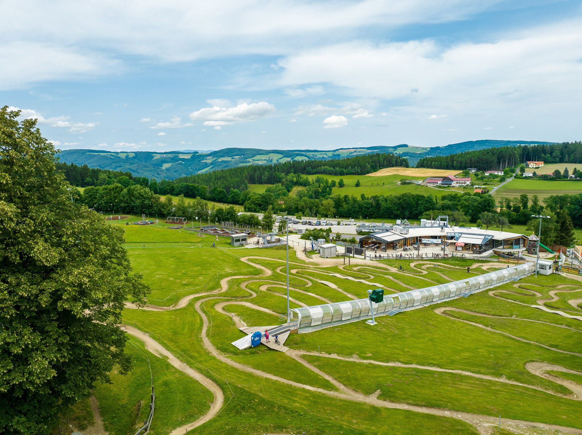 Luftaufnahme der Wexl Arena in St. Corona am Wechsel mit grünen Hügeln und einem Gebäude im Hintergrund.