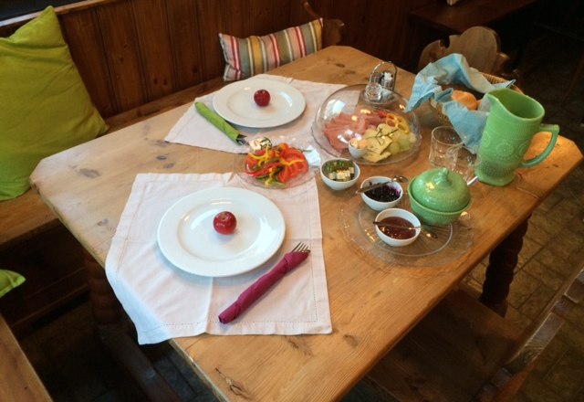 Ein gedeckter Frühstückstisch mit Tellern, Besteck, Aufschnitt, Gemüse und Getränken.