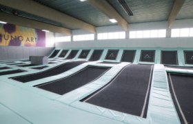 Innenansicht eines Trampolinparks mit mehreren Trampolinen in einer Halle.