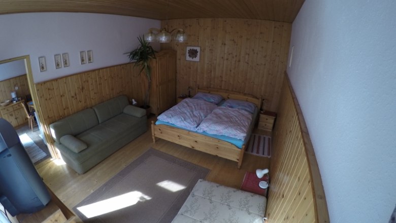 Ein gemütliches Schlafzimmer mit Holzwänden, einem Doppelbett, einem Sofa und einem Teppich auf Holzboden.
