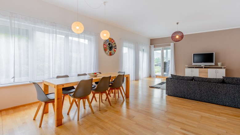 Moderner Essbereich mit Holztisch, grauen Stühlen und großer Fensterfront.