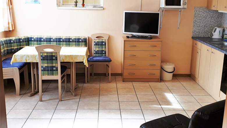 Küche, © Stern Küche mit Eckbank, Tisch, Stühlen, Fernseher, Mikrowelle und Schränken.