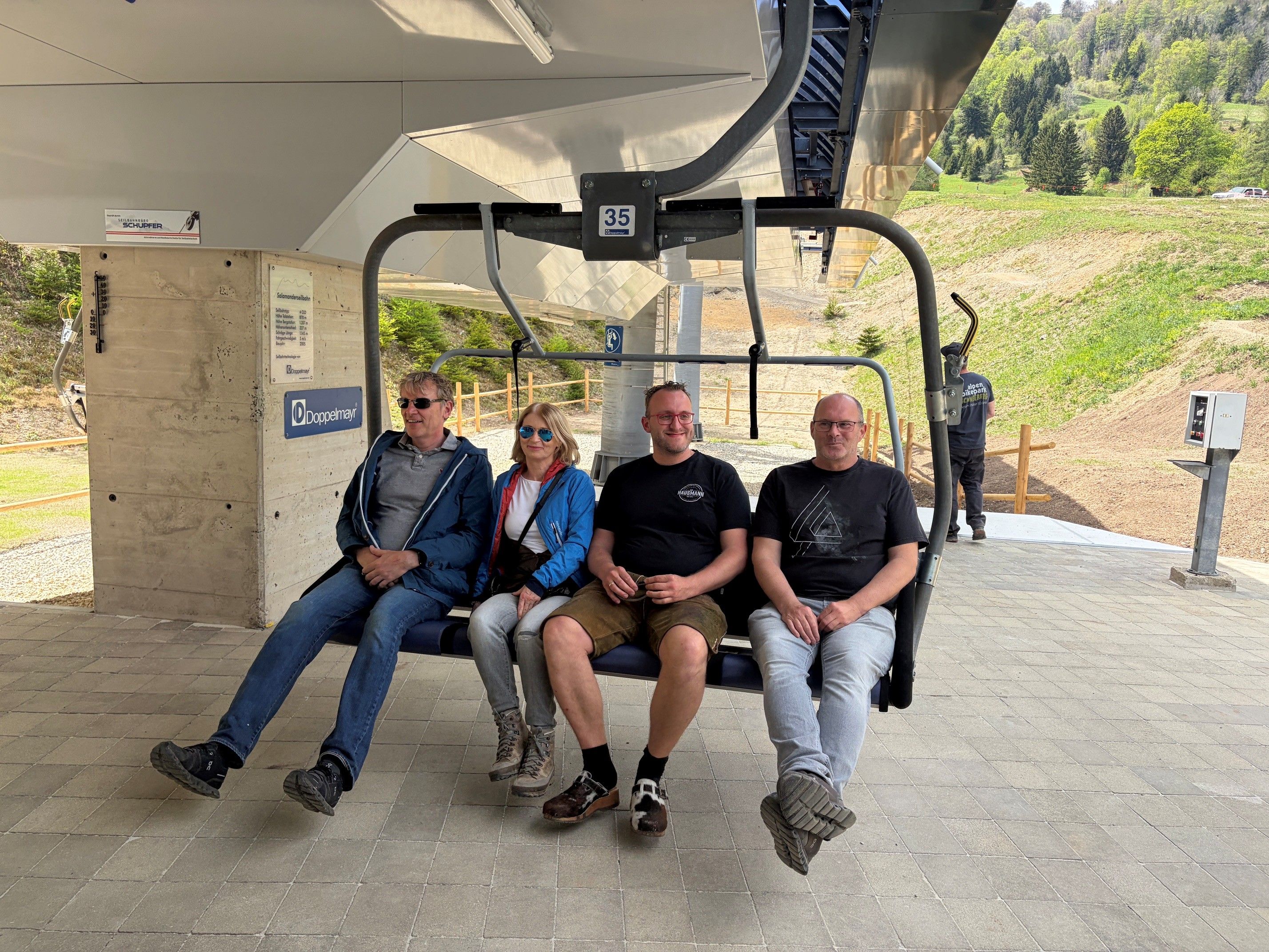 Vier Personen sitzen auf einem Sessellift in der Sessellift-Station.