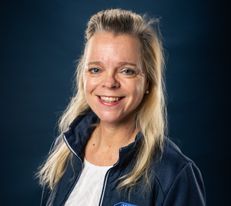 Portraitfoto Wiener Alpen Mitarbeiterin, die eine Jacke mit Wiener Alpen Logo trägt und vor einem dunklem Hintergrund steht.