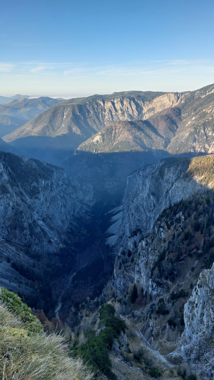 Blick auf eine tiefe Schlucht mit steilen Felswänden und bewaldeten Bergen im Hintergrund unter klarem Himmel.