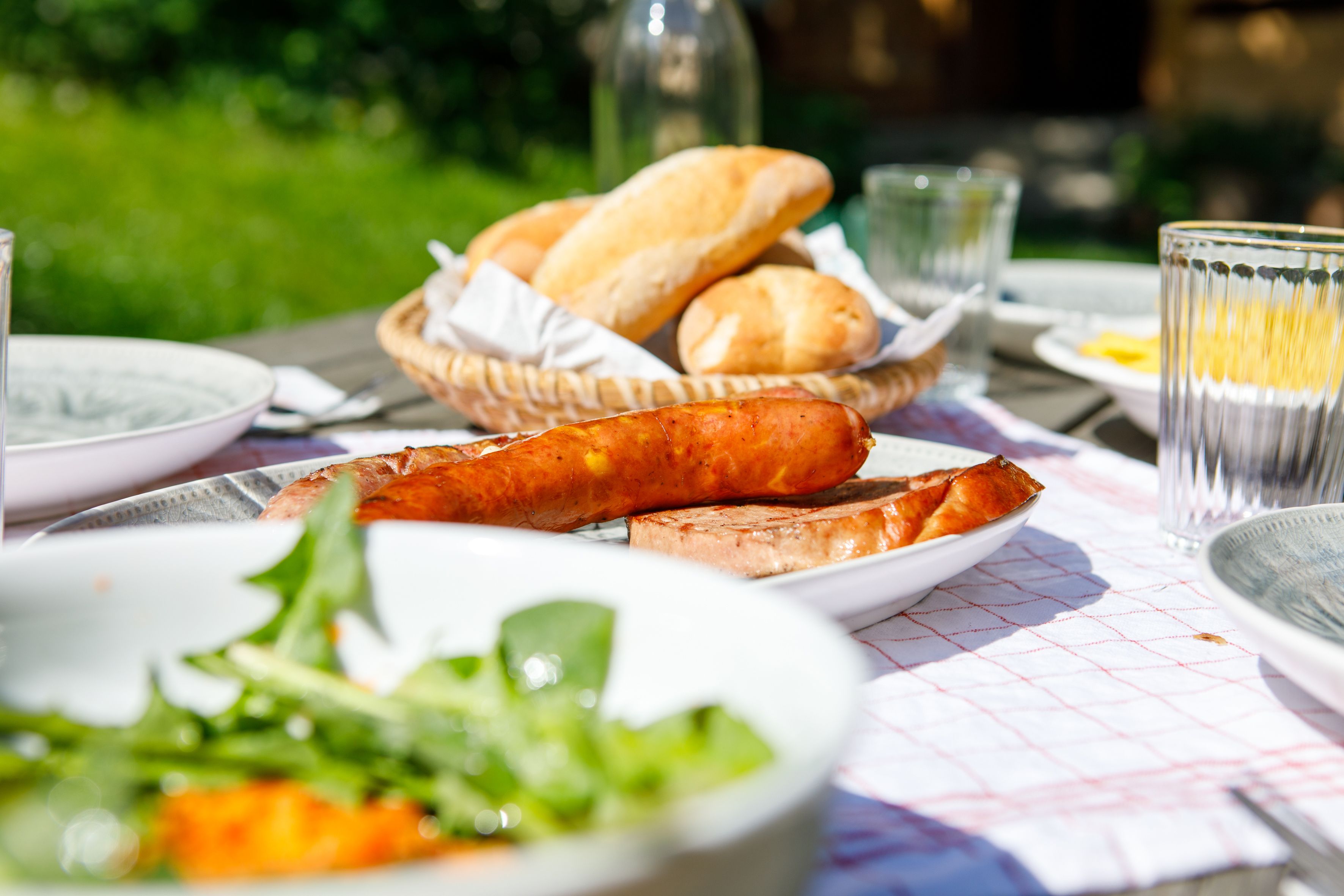 Ein Tisch im Freien mit Brot, Wurst und Salat.