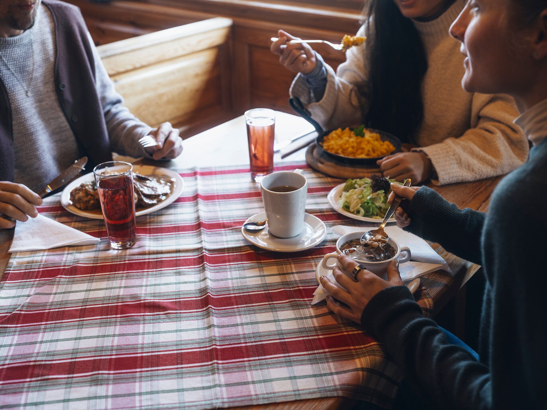 Inmitten der winterlichen Landschaft genießen Freunde ein herzhaftes Mahl, während dampfender Kaffee und frische Salate den Tisch zieren. Die gemütliche Atmosphäre und das knisternde Holzfeuer laden dazu ein, die Seele baumeln zu lassen und die winterliche Idylle der Wiener Alpen zu erleben.