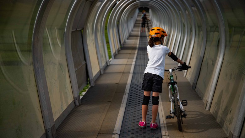Kind mit Fahrrad auf Förderband im überdachten Tunnel.