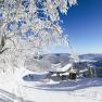 Winterlandschaft mit Sesselliftstation, verschneiten Bäumen und Bergen im Hintergrund.