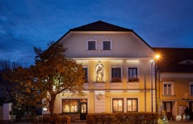 Gasthaus St. Florian bei Dämmerung mit beleuchteter Fassade und Statue.