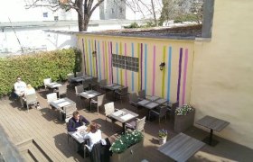 Au&szlig;enbereich eines Caf&eacute;s mit bunten Streifen an der Wand und mehreren Tischen.