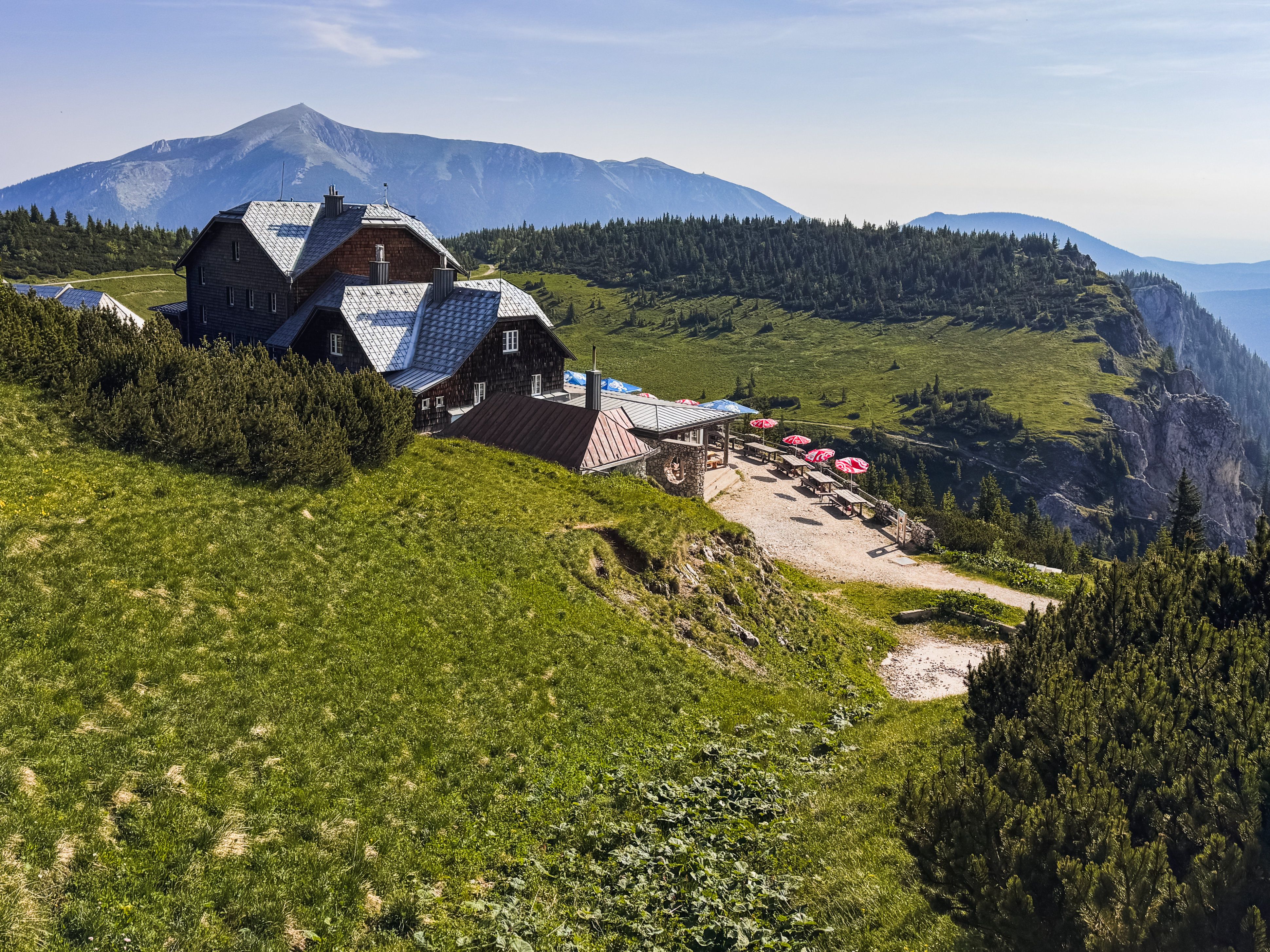 Berglandschaft mit dem Ottohaus auf der Rax, umgeben von grünen Wiesen und einem Berg im Hintergrund.