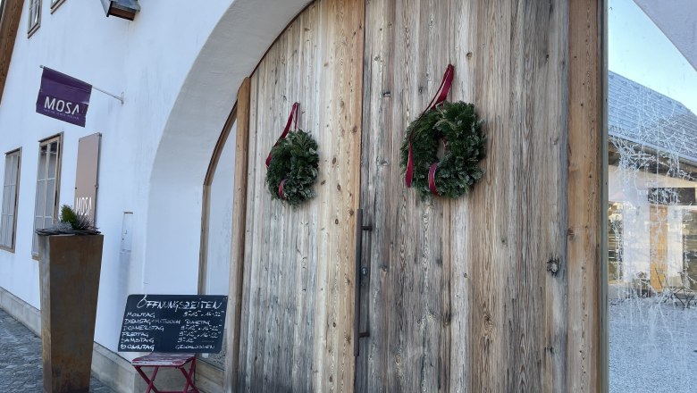 Eingang der Cafe-Bar Mosa mit Holztür und Kränzen.
