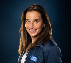Portraitfoto Wiener Alpen Geschäftsführerin, die eine Jacke mit Wiener Alpen Logo trägt und vor einem dunklem Hintergrund steht.