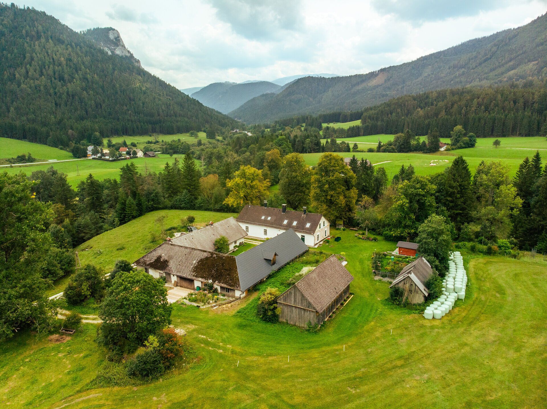 Der Höblinghof in Schwarzau im Gebirge liegt inmitten der Berge. Im Garten wird Gemüse angebaut, Ein Liegestuhl steht inmitten der Wiese und vor dem Haus, der zum Verweilen einlädt.