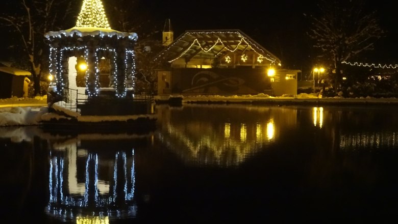 Weihnachtlich beleuchteter Pavillon am See in Puchberg bei Nacht.